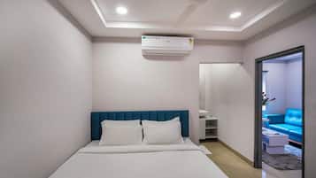 Una habitación de hotel con una cama, un ventilador de techo, aire acondicionado y vistas a un sofá azul en la habitación contigua.