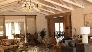 A spacious living area with a high ceiling, exposed beams, and a large chandelier. There is a dining area with a table and chairs, and a seating area with sofas and a coffee table. - Vyge Valley Estate (Cape Town)