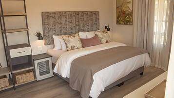 A bedroom with a bed, bedside tables, a headboard, a nightstand, a wall art piece, and a window with curtains.