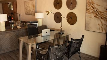 A modern dining area with a glass table, black woven chairs, and decorative wall clocks.