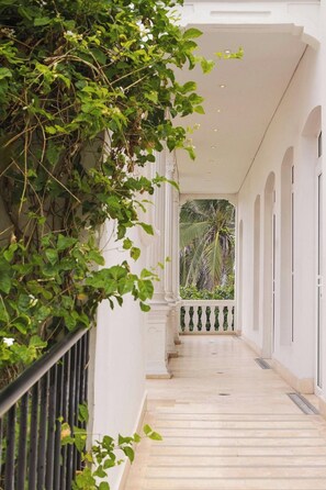 A corridor with a white balustrade, columns, and a view of greenery in the distance. - Ermita Cartagena, A Tribute Portfolio Hotel (Cartagena)