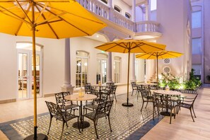 A spacious indoor patio with multiple tables and chairs, large yellow umbrellas, and a balcony with white balustrades. - Ermita Cartagena, A Tribute Portfolio Hotel (Cartagena)