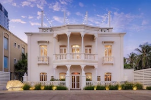 A large, white, two-story building with a central entrance, balconies, and a decorative roof.