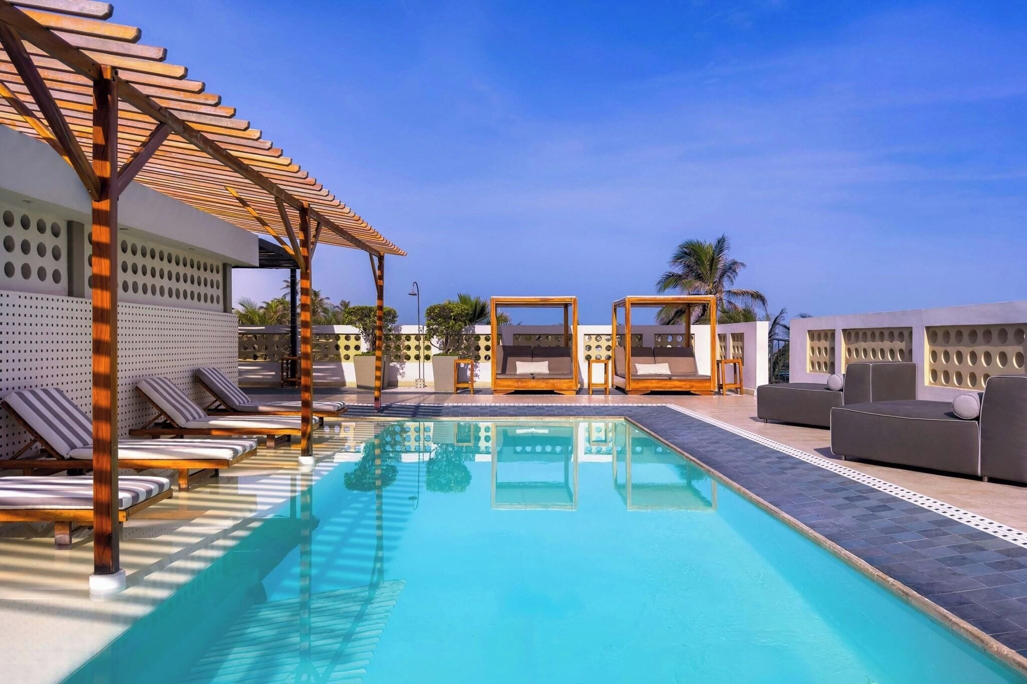 A pool area with lounge chairs, a wooden pergola, and a clear blue sky.