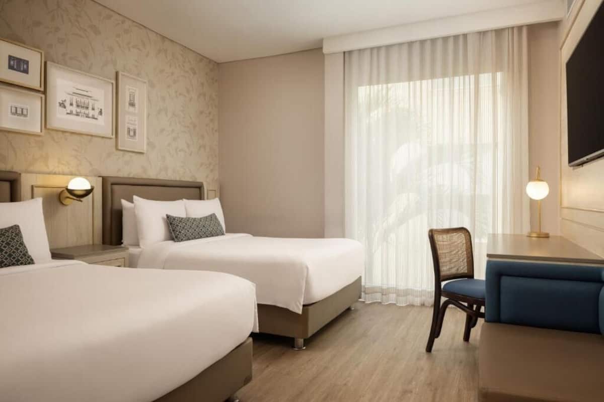 Habitación de hotel con dos camas, un escritorio, una silla y un televisor.
