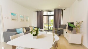 Een moderne woonkamer met een witte eettafel, een grijze bank en een televisie op een wit kastje.