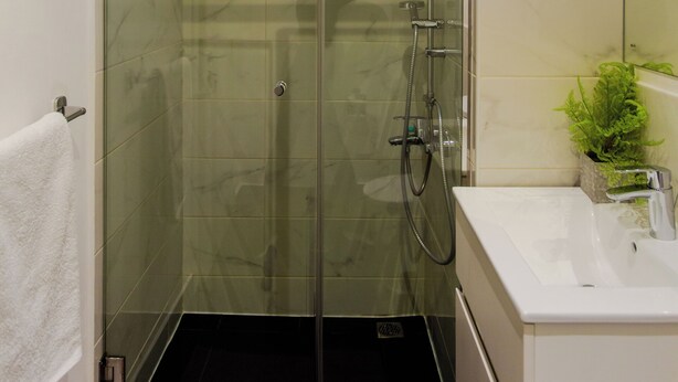 A glass-enclosed shower stall with a handheld showerhead and a wall-mounted faucet. - Accra Luxury Apartments At Embassy Gardens (Accra)
