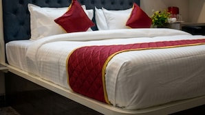 A bed with a tufted headboard, white bedding, red and gold accents, and a bedside table with a vase of flowers.