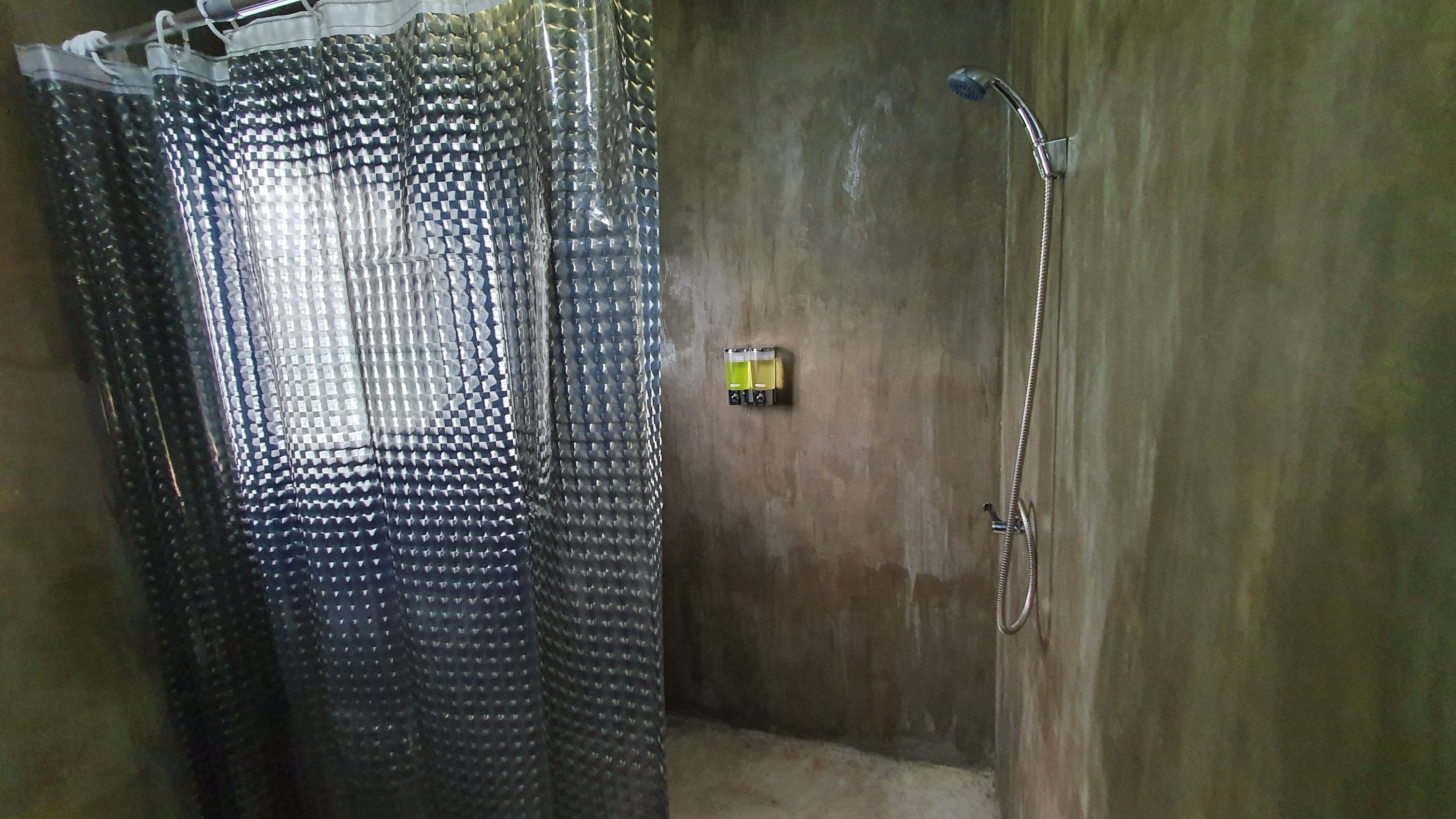 Un área de ducha con cortina, cabezal de ducha de mano y panel de control en la pared.