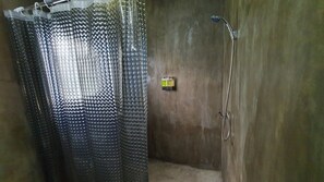 Un área de ducha con cortina, cabezal de ducha de mano y panel de control en la pared.