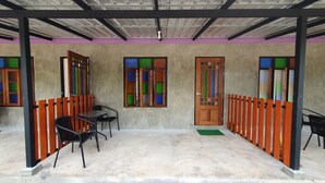 A covered outdoor seating area with a concrete floor, wooden door, and colorful window panes. - Moonshine Resort Chumphon (Chumphon)