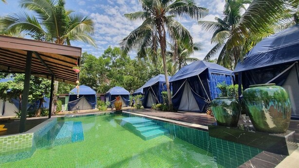 A pool area with clear water, surrounded by palm trees and blue tents. - Moonshine Resort Chumphon (Chumphon)