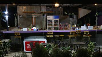 Zona de bar con refrigerador, asientos y plantas colgantes.