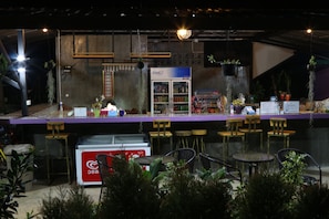 A bar area with a refrigerator, seating, and hanging plants.