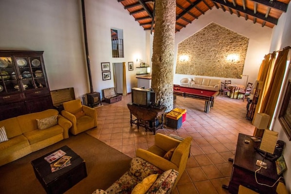 A cozy living room with a fireplace, yellow sofas, a wooden cabinet, and a stone wall. - Quinta Da Alcaidaria-mór (Ourem)