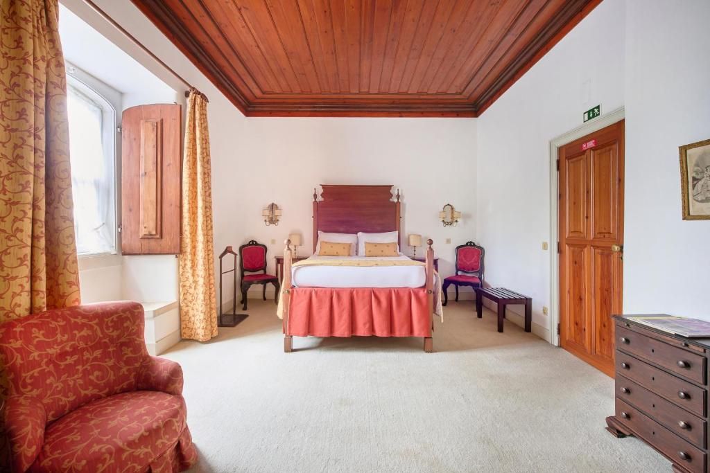 Une chambre avec un plafond en bois, un lit avec une tête de lit, une chaise, une commode et une porte avec une pancarte.