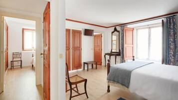 A bedroom with a bed, wooden wardrobe, a small table, a chair, and a television.