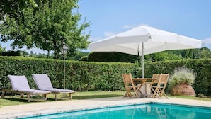 Une piscine avec des chaises longues et une table munie d’un parasol.