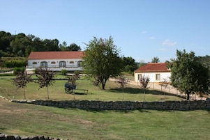 A white building with a red roof, surrounded by a stone wall, trees, and a bench.