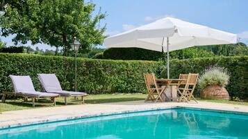 A swimming pool with lounge chairs and a table with an umbrella.