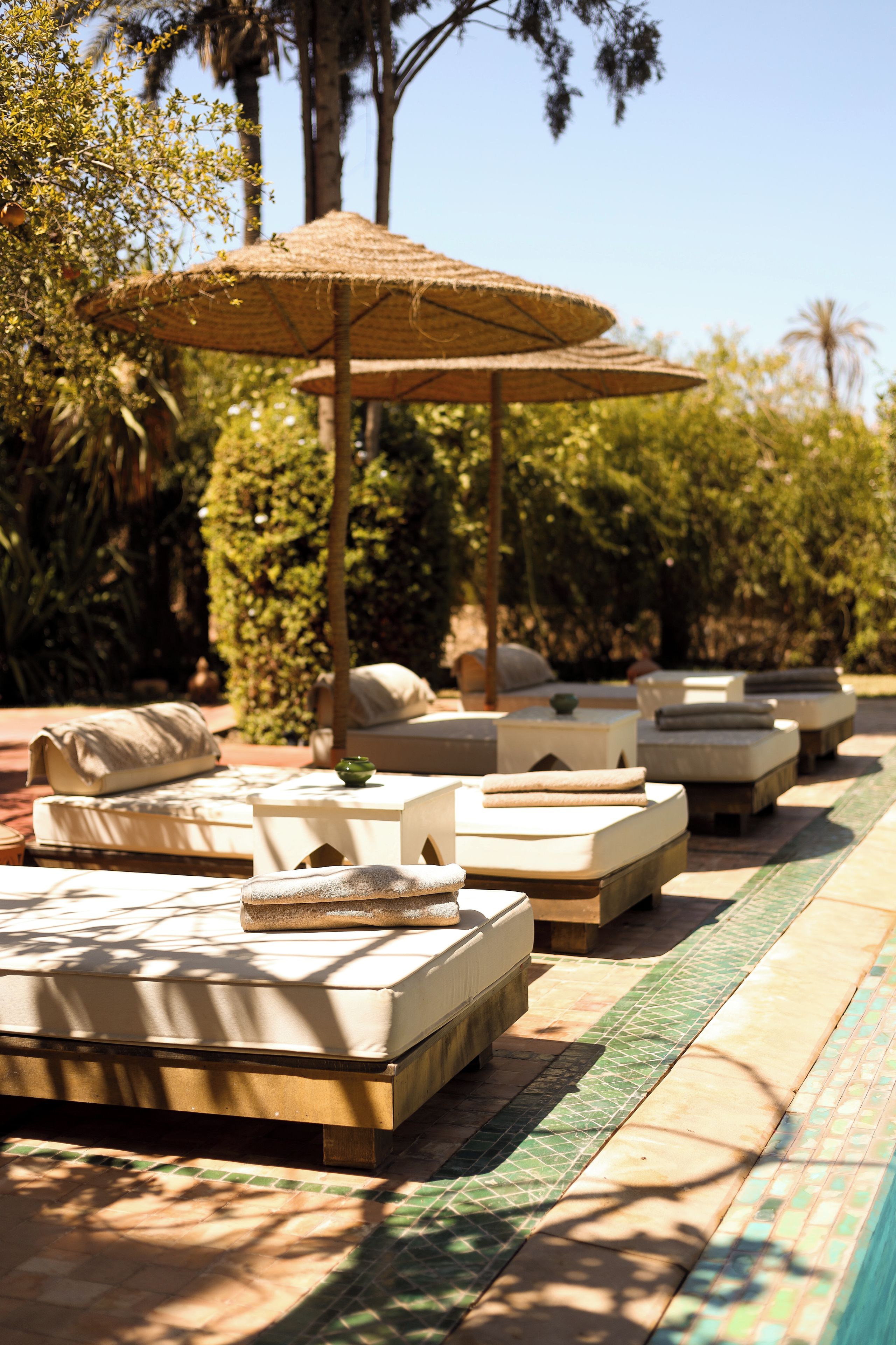 A poolside area with lounge chairs and umbrellas, surrounded by greenery.