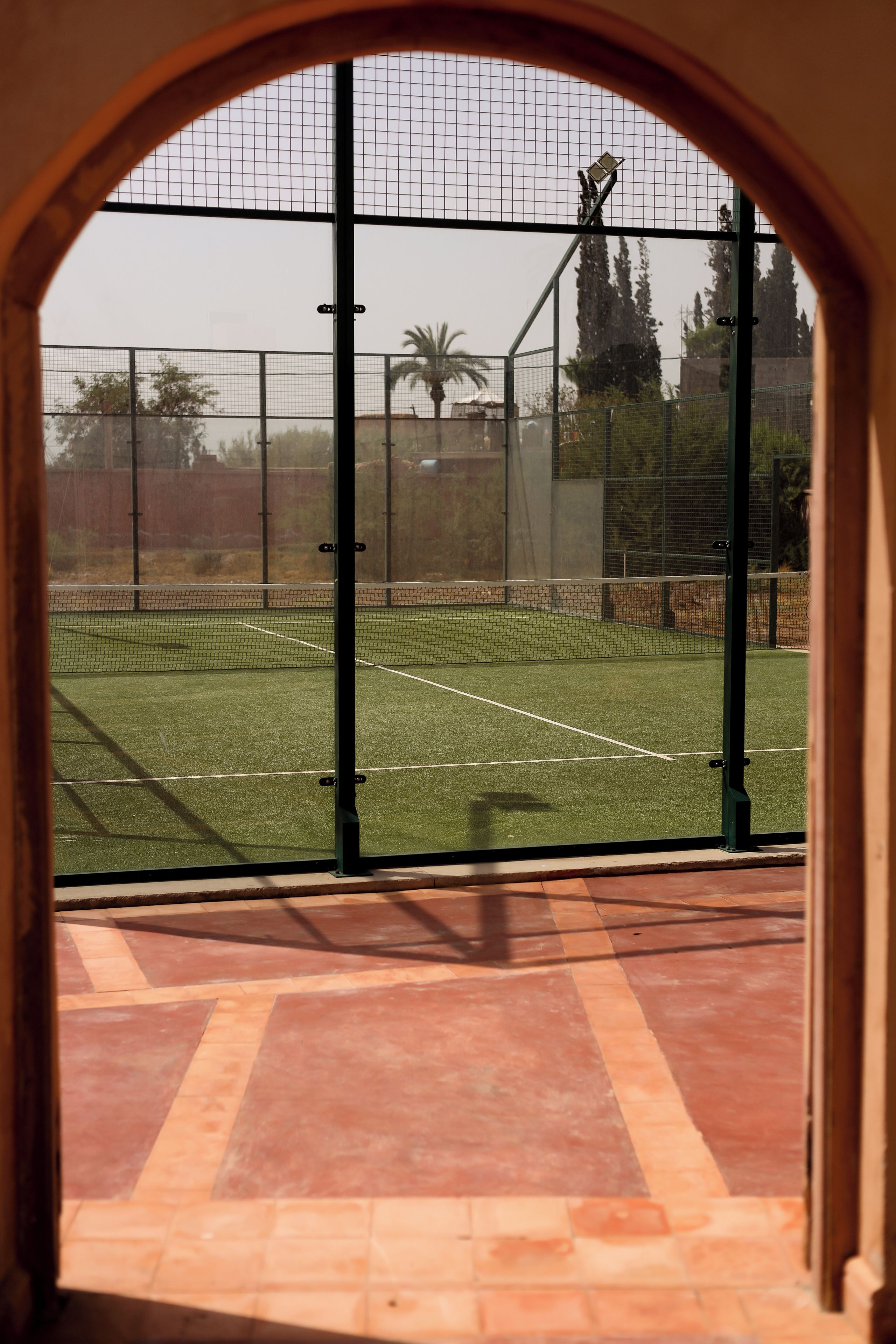 An indoor tennis court with a net, surrounded by a fence, and viewed through an arched doorway.