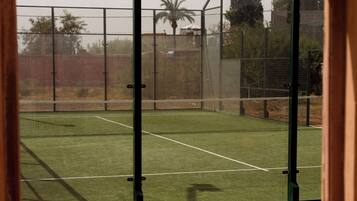 An indoor tennis court with a net, surrounded by a fence, and viewed through an arched doorway.