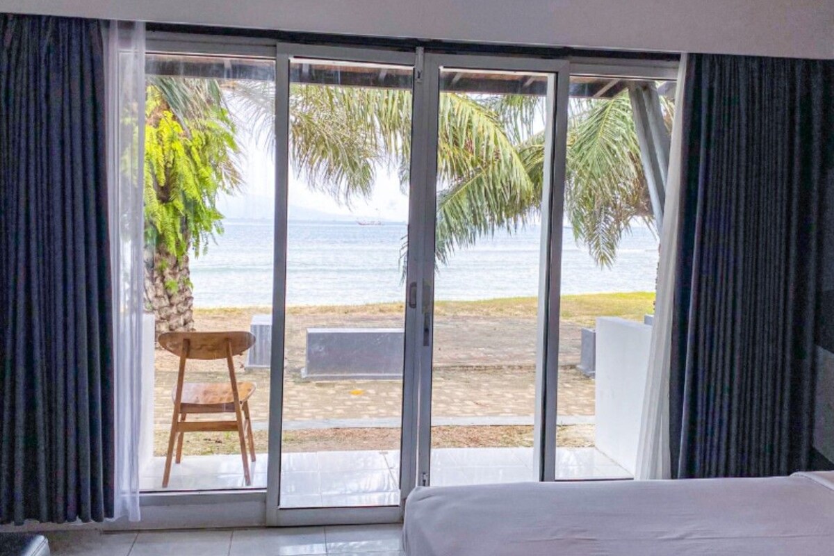 Una habitación con cama, vista a la playa y una silla afuera.