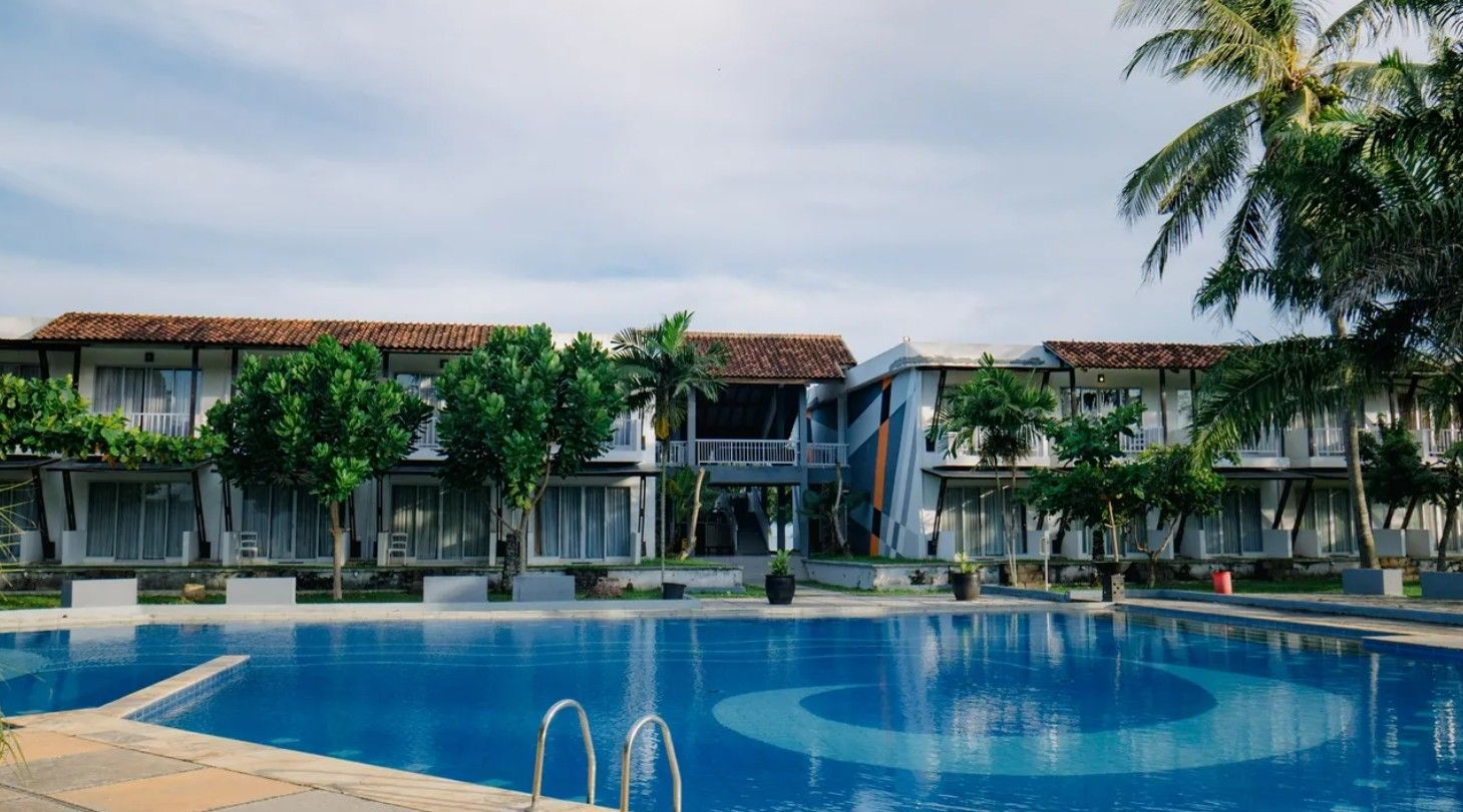 A hotel with a swimming pool, multiple balconies, and tropical landscaping.