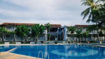 A hotel with a swimming pool, multiple balconies, and tropical landscaping.