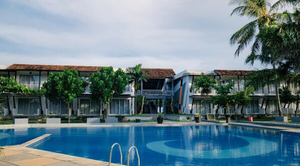 Un hotel con piscina, varios balcones y jardines tropicales.