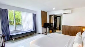 Habitación de hotel con una cama grande, un banco junto a la ventana, un escritorio con una silla y un equipo de aire acondicionado.