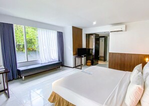 Habitación de hotel con una cama grande, un banco junto a la ventana, un escritorio con una silla y un equipo de aire acondicionado.