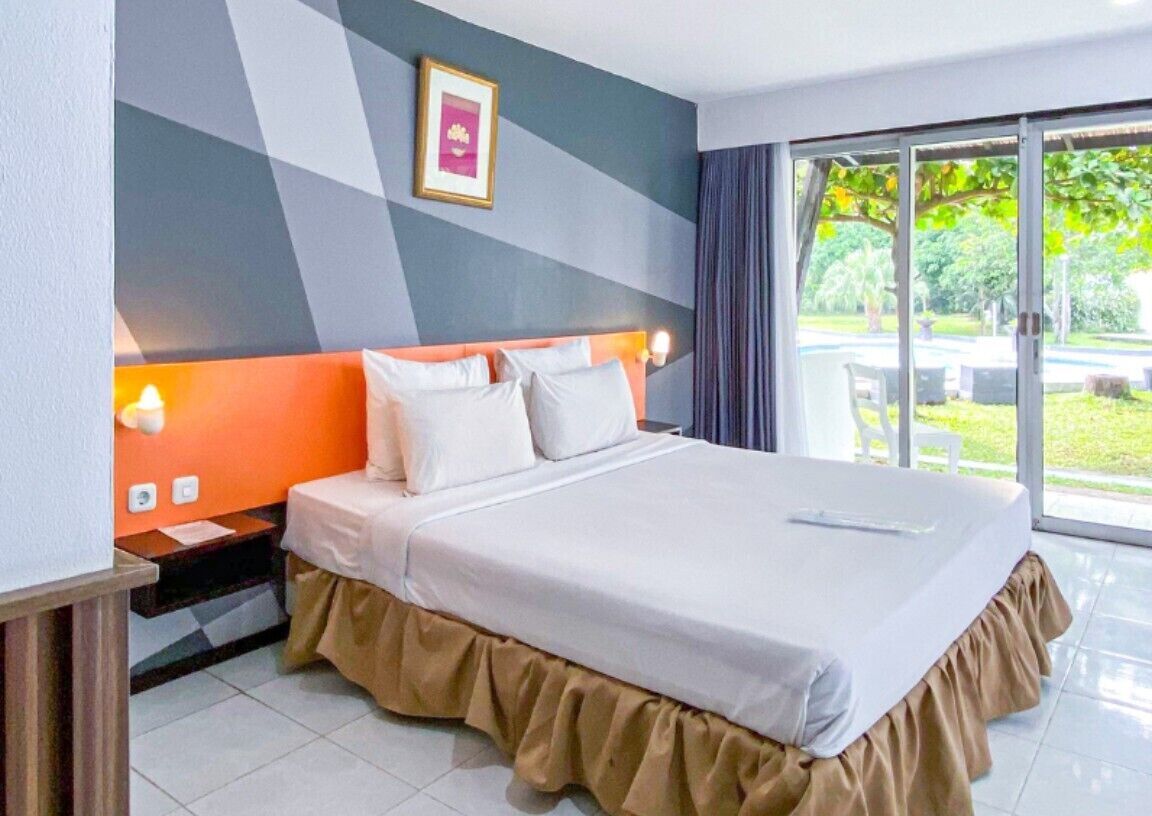 Habitación de hotel con cama, mesita de noche, ventana y vista a follaje, además de una pared con diseño geométrico.