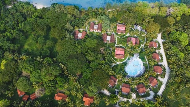 Vista aérea de un resort con varias cabañas, una piscina central y densa vegetación tropical circundante.
