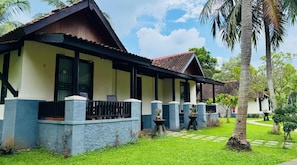 A two-story building with a balcony, a tiled roof, and a well-maintained lawn with palm trees.