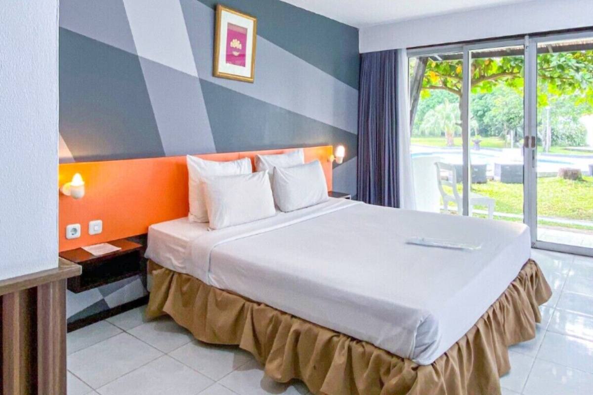 Habitación de hotel con cama, mesita de noche, ventana y vista a follaje, además de una pared con diseño geométrico.