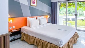 Habitación de hotel con cama, mesita de noche, ventana y vista a follaje, además de una pared con diseño geométrico.