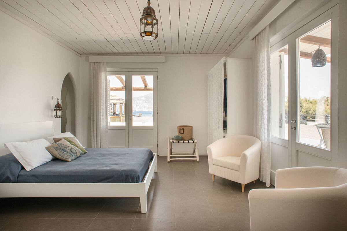 Un dormitorio con cama, una silla, una mesita y ventana con vistas.