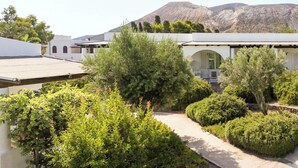 A building with a white facade, a covered patio area, and a pathway surrounded by greenery. - Hotiday Vulcano Porto  (Lipari)