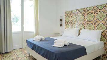 Una camera d'albergo con un letto, una finestra con tende, una parete decorata e un comodino.