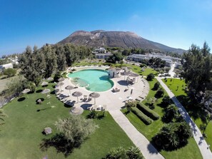 Un resort con piscina central, zonas de descanso y montañas al fondo.