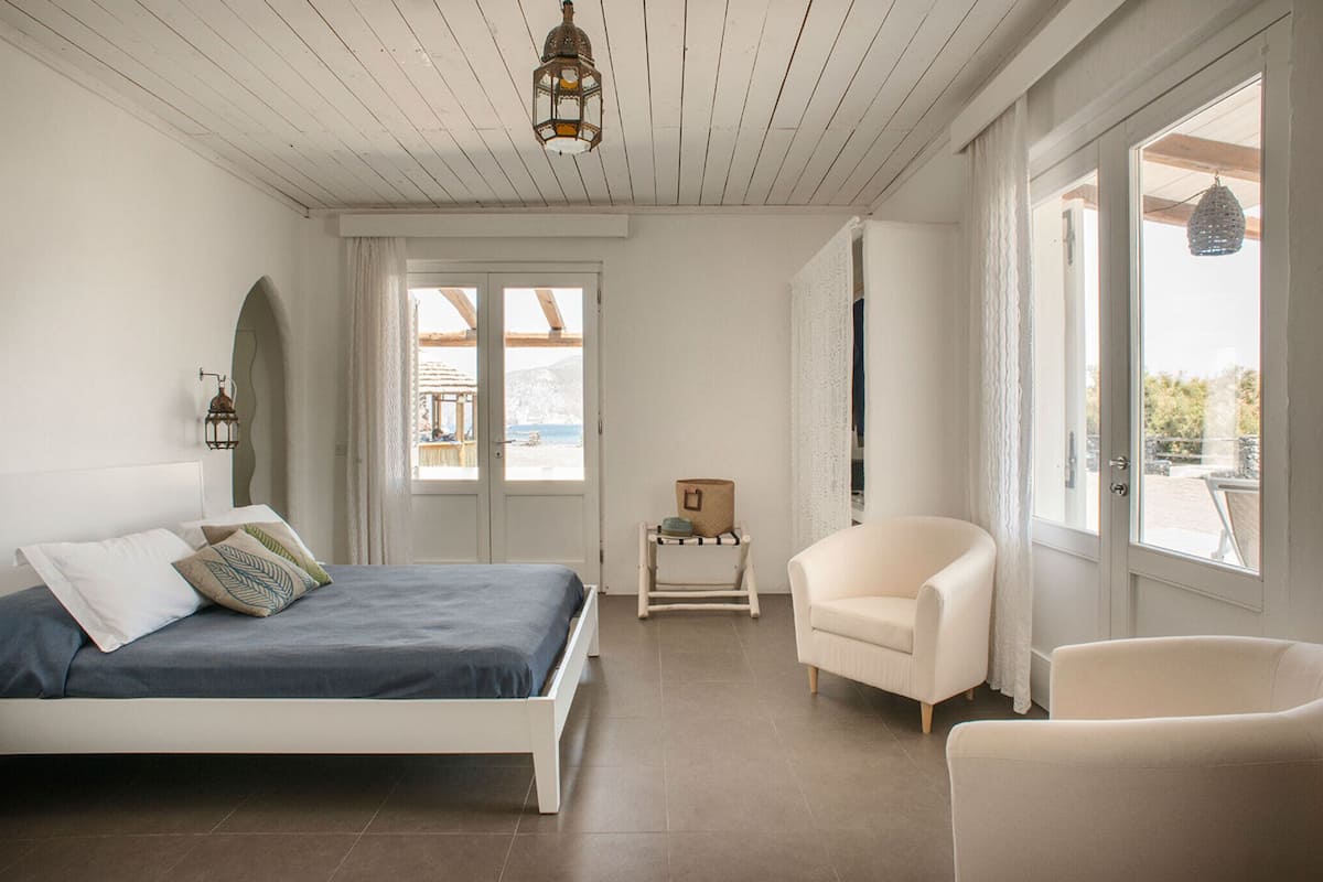 Un dormitorio con cama, una silla, una mesita y ventana con vistas.