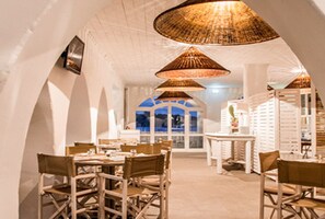 A dining area with wicker lamps, white walls, and a view through a window.