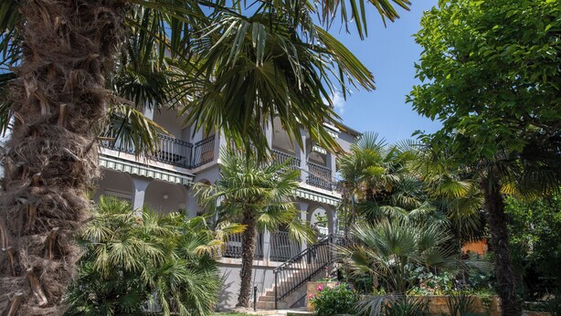 Un edificio de varios pisos con balcones, rodeado de palmeras y un jardín cuidado.