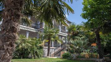 A multi-story building with balconies, surrounded by palm trees and a well-maintained garden.
