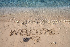 Una playa con las palabras 'WELCOME' y un corazón dibujado en la arena.