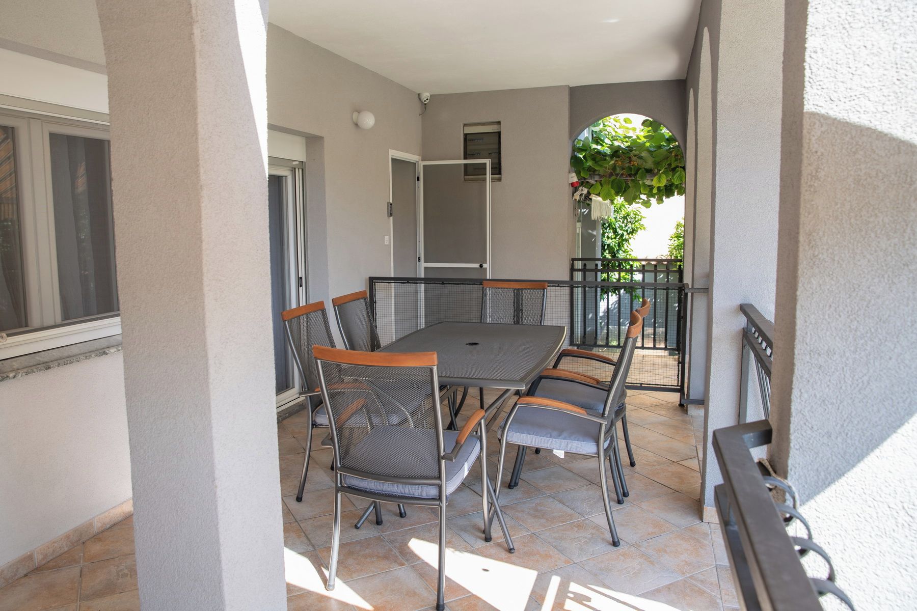 En balkon med et bord og stole, et overvågningskamera og udsigt til en bygning.