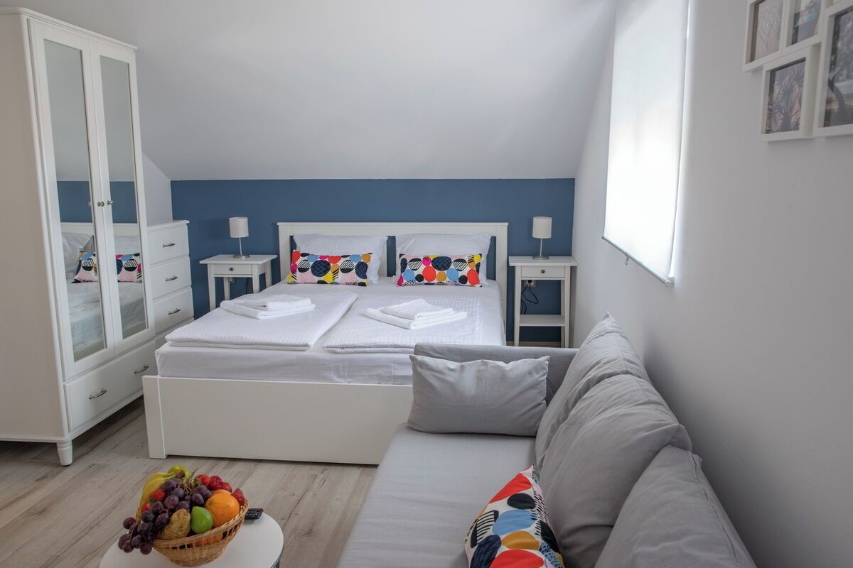 A bedroom with a bed, a bedside table, a wardrobe, a sofa, and a fruit bowl.