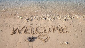 Una playa con las palabras 'WELCOME' y un corazón dibujado en la arena.
